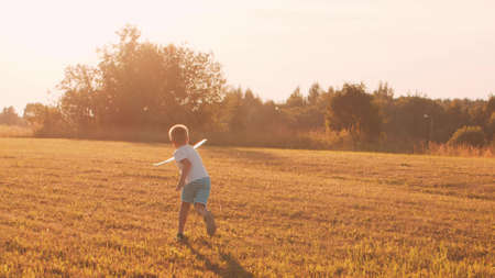 Boy plays with a toy plane in a field at sunset. The concept of childhood, freedom and inspiration.の写真素材
