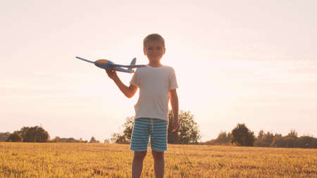 Boy plays with a toy plane in a field at sunset. The concept of childhood, freedom and inspiration.の写真素材