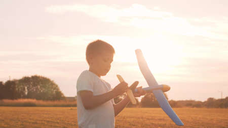 Boy plays with a toy plane in a field at sunset. The concept of childhood, freedom and inspiration.の写真素材