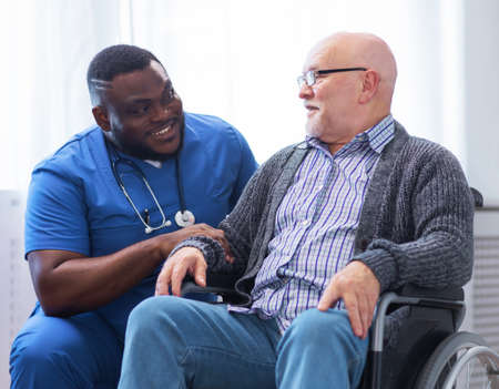 Professional doctor helps an elderly man with chronic diseases. Therapist and patient in home interior. Health care and medicine concept.の写真素材