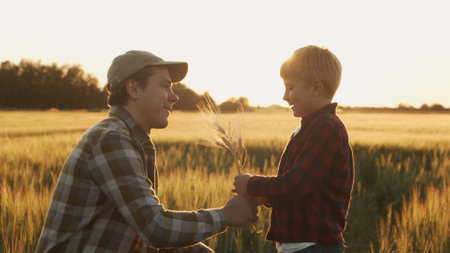 Farmer and his son in front of a sunset agricultural landscape. Man and a boy in a countryside field. Fatherhood, country life, farming and country lifestyle.の写真素材