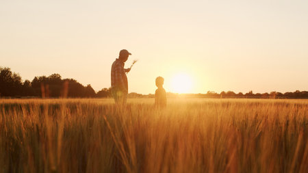 Farmer and his son in front of a sunset agricultural landscape. Man and a boy in a countryside...
