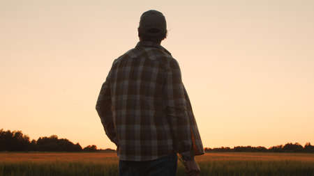 Farmer in front of a sunset agricultural landscape. Man in a countryside field. Country life, food production, farming and country lifestyle concept.の写真素材