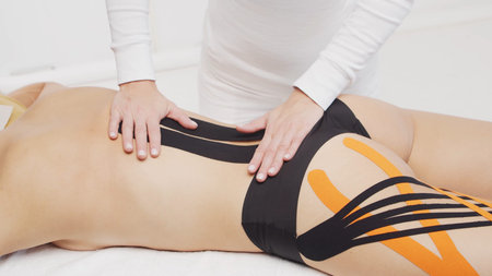 Therapist is applying tape to female body. Physiotherapy, kinesiology and recovery treatment.