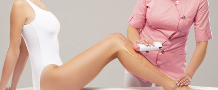 Beautician is removing hair from young female body and legs with hot wax. Woman has a beauty...