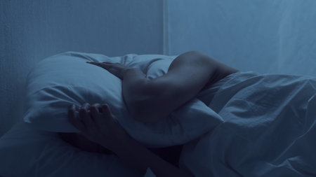 Young woman lying in the bed at night and having insomnia disease. Beautiful blond sleeping girl. Twilight in the bedroom, moonlight from the window. Sleeplessness, health and rest concept.の写真素材
