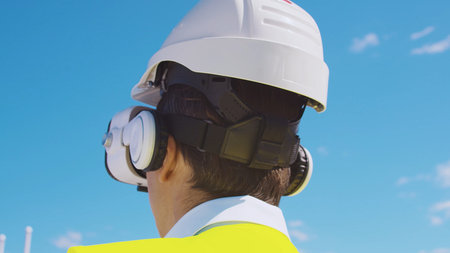 Professional builder in VR helmet standing in front of construction site and using virtual and...