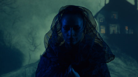 Beautiful witch making the witchcraft over the smoky background at night. Scary house on the hill....