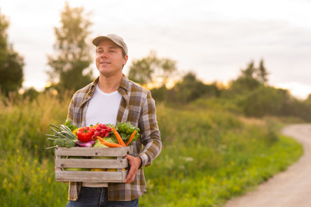 Farmer with a vegetable box in front of a sunset agricultural landscape. Man in a countryside field. Country life, food production, farming and country lifestyle concept.の写真素材