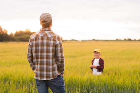 Farmer and his son in front of a sunset agricultural landscape. Man and a boy in a countryside field. Fatherhood, country life, farming and country lifestyle concept.の写真素材