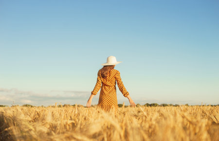Beautiful young woman walks across the field and touches rye with her hand. Girl in the rays of the sunset. Freedom and happiness concept.の写真素材
