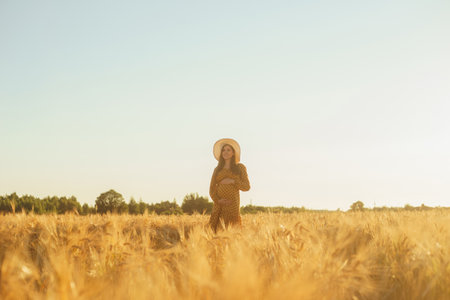 Pregnant woman in the rays of the sunset. Beautiful young girl is walking in the field expecting the birth of a child. Motherhood, pregnancy and happiness concept.の写真素材