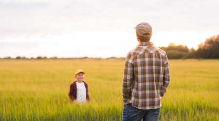 Farmer and his son in front of a sunset agricultural landscape. Man and a boy in a countryside field. Fatherhood, country life, farming and country lifestyle concept.の写真素材