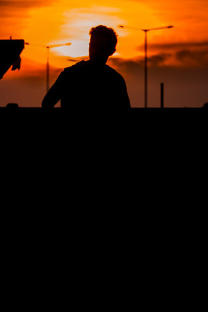 Silhouette of a young man standing in the city at sunsetの写真素材