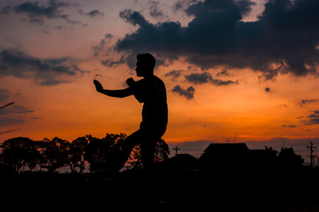 Silhouette of a young man jumping in the sunset sky.の写真素材