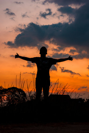 Silhouette of young man with arms outstretched at sunset.の写真素材