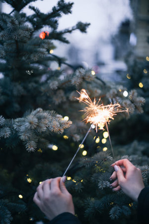womans hand holding sparklers on the background of a Christmas tree with lightsの写真素材