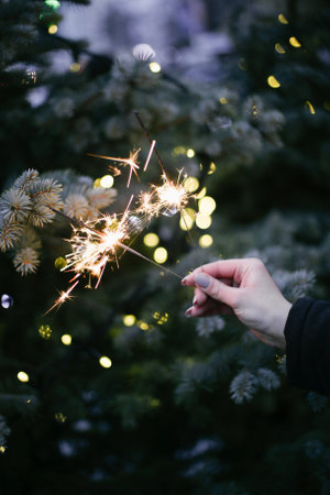 girls hand holding sparklers on the background of a Christmas tree with lightsの写真素材