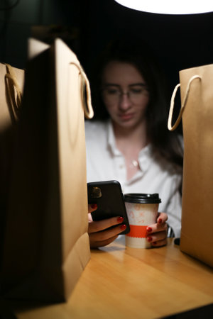 a young woman sits among paper bags with purchases and looks at the phone.の写真素材