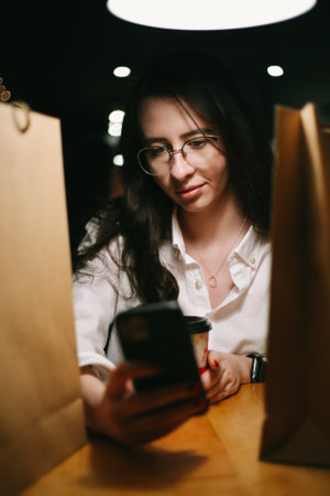 a young woman sits among paper bags with purchases and looks at the phoneの写真素材