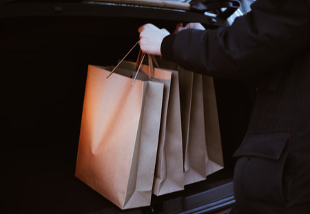 a young man puts paper shopping bags in the trunk of a carの写真素材