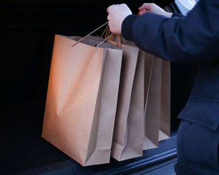 a young man puts paper shopping bags in the trunk of a carの写真素材
