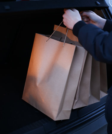 a young man puts paper shopping bags in the trunk of a carの写真素材