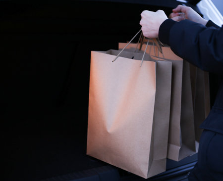 a young man puts paper shopping bags in the trunk of a carの写真素材