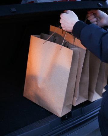 a young man puts paper shopping bags in the trunk of a carの写真素材