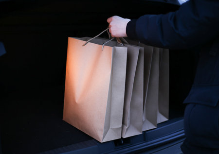 a young man puts paper shopping bags in the trunk of a carの写真素材