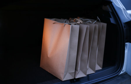 a young man puts paper shopping bags in the trunk of a carの写真素材