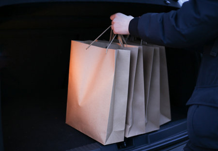 a young man puts paper shopping bags in the trunk of a carの写真素材