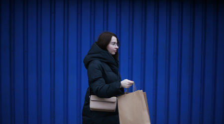 young woman in winter clothes with paper bags with purchases on blue backgroundの写真素材