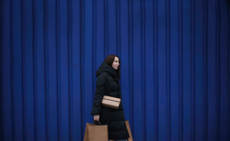 young woman in winter clothes with paper bags with purchases on blue backgroundの写真素材