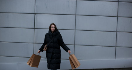 young woman in winter clothes with paper bags with purchases on grey backgroundの写真素材