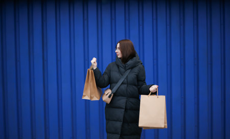 young woman in winter clothes with paper bags with purchases on blue backgroundの写真素材