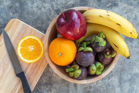 Cutting orange on wooden board with multi fruit in wooden bowl frome top view.