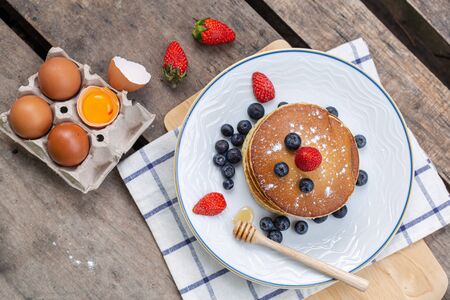 Pancake with fresh berries on white plate with eggs on old wood background, top viewの写真素材