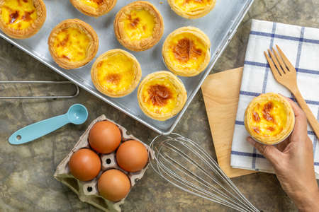dessert egg tart or portugal egg tart sweet custard cream on wooden board and bright gray concrete background with eggs ingredient and cooking tools, top viewの写真素材