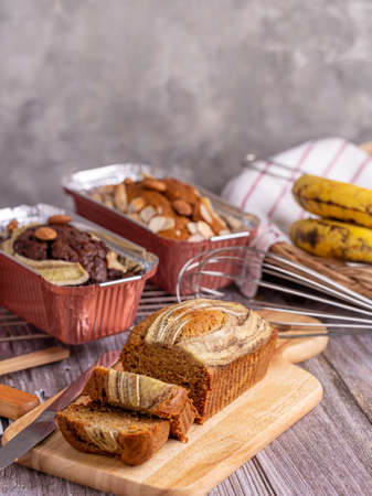Homemade banana bread sliced on a wooden board with banana bread in loaf foil on the table.の写真素材