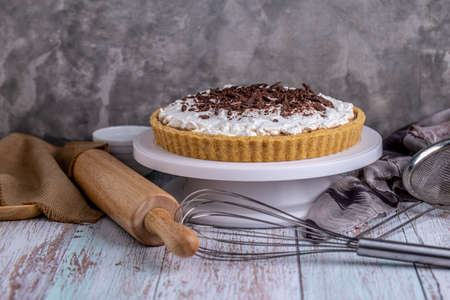 Homemade Banoffee pie with caramel, banana and chocolate topping with cooking tools on table.の写真素材