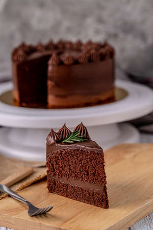 Slice of delicious homemade chocolate cake soft fudge paste on wooden board with fork for serve.の写真素材