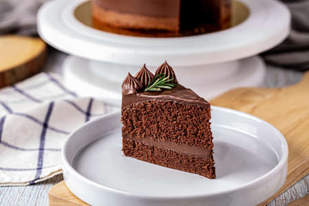 Slice of delicious homemade chocolate cake soft fudge topping with rosemary on white plate.の写真素材