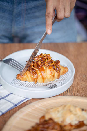 Lady use knife with almond caramel croissants on breakfast table.の写真素材