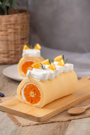 Orange roll cake topping with fresh cream orange and rosemary paste on wooden board.の写真素材