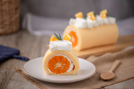 Orange roll cake topping with fresh cream orange and rosemary paste on white plate.の写真素材