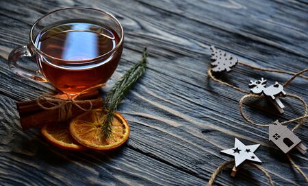 Cup of tea, dried slices of orange and cinnamon sticks with Christmas decorations on a dark wooden background. Festive background.の写真素材