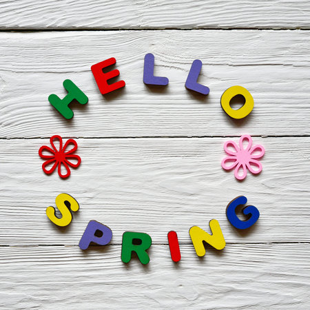 Multi-colored wooden letters making up the words Hello spring and multi-colored wooden flowers on a...