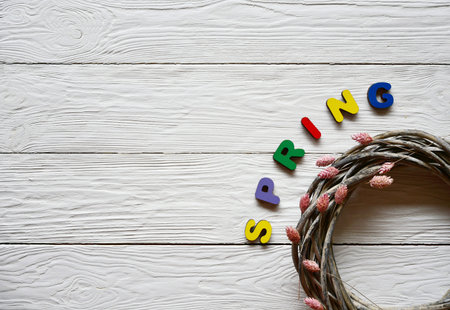 Multi-colored wooden letters making up the word Spring and rattan wreath with dried flowers on a...