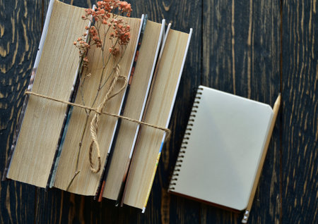 A stack of books tied with twine, dried flowers and notebook with pencil on a dark wooden...